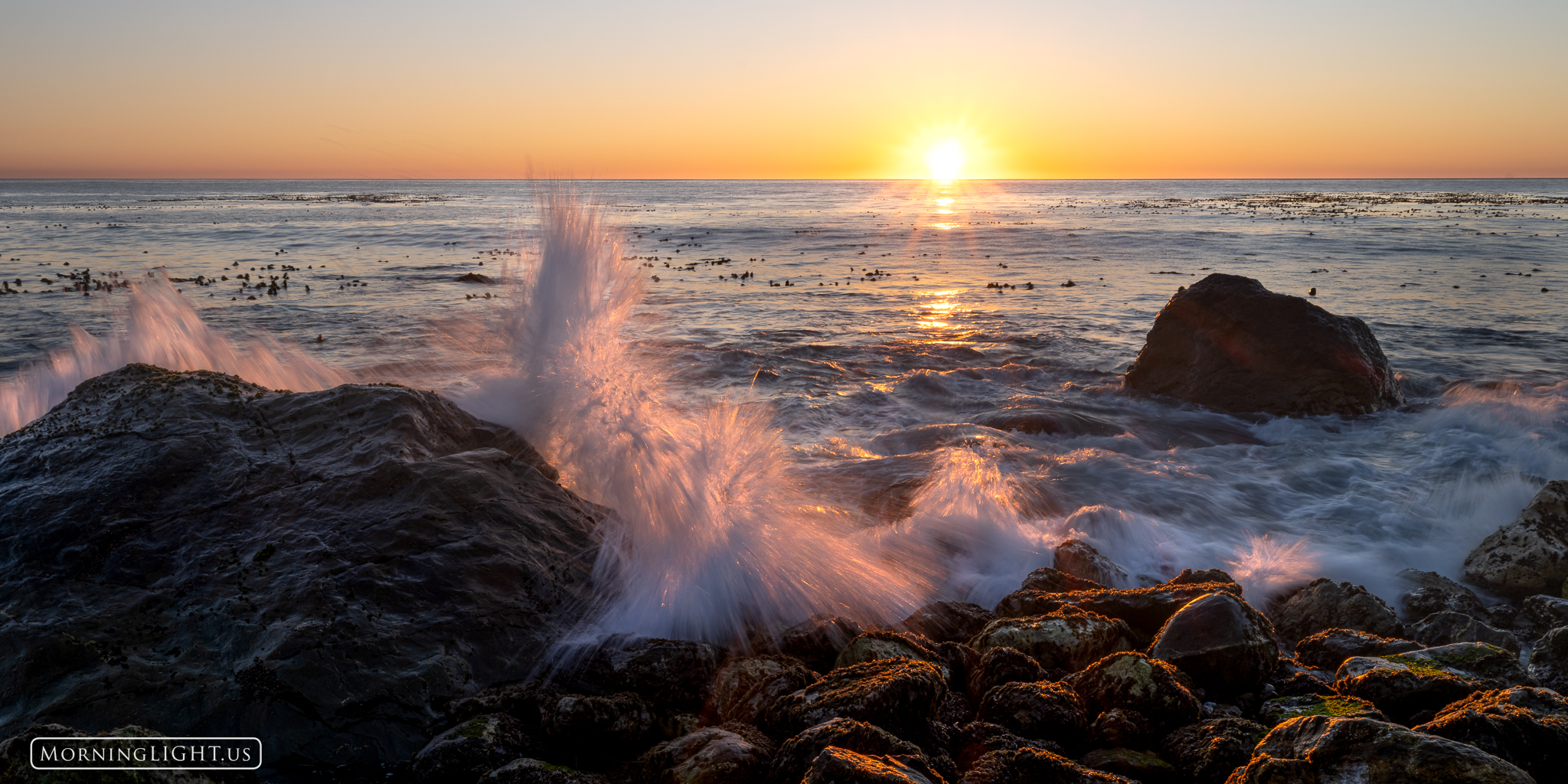 Gentle waves roll in and crash against the rocks on a perfect evening on California's Pacific Coast.