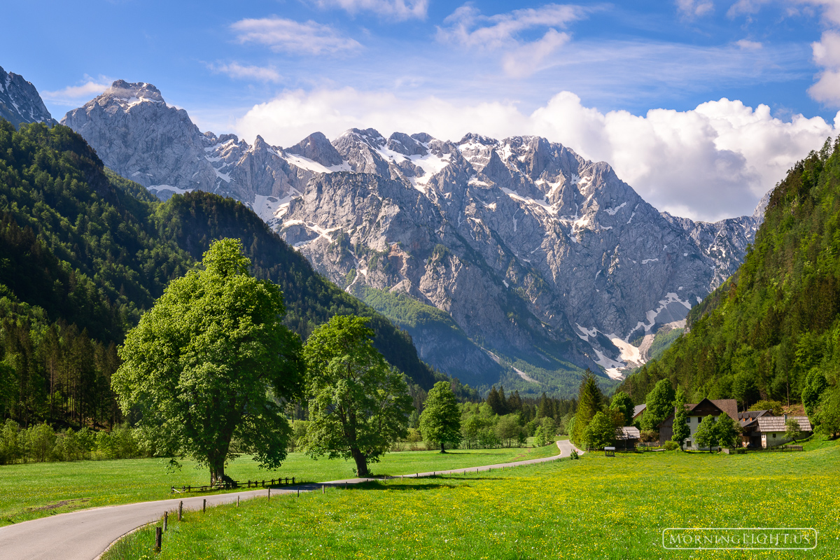 The jagged Julian Alps rise high over a farmstead in Slovenia.
