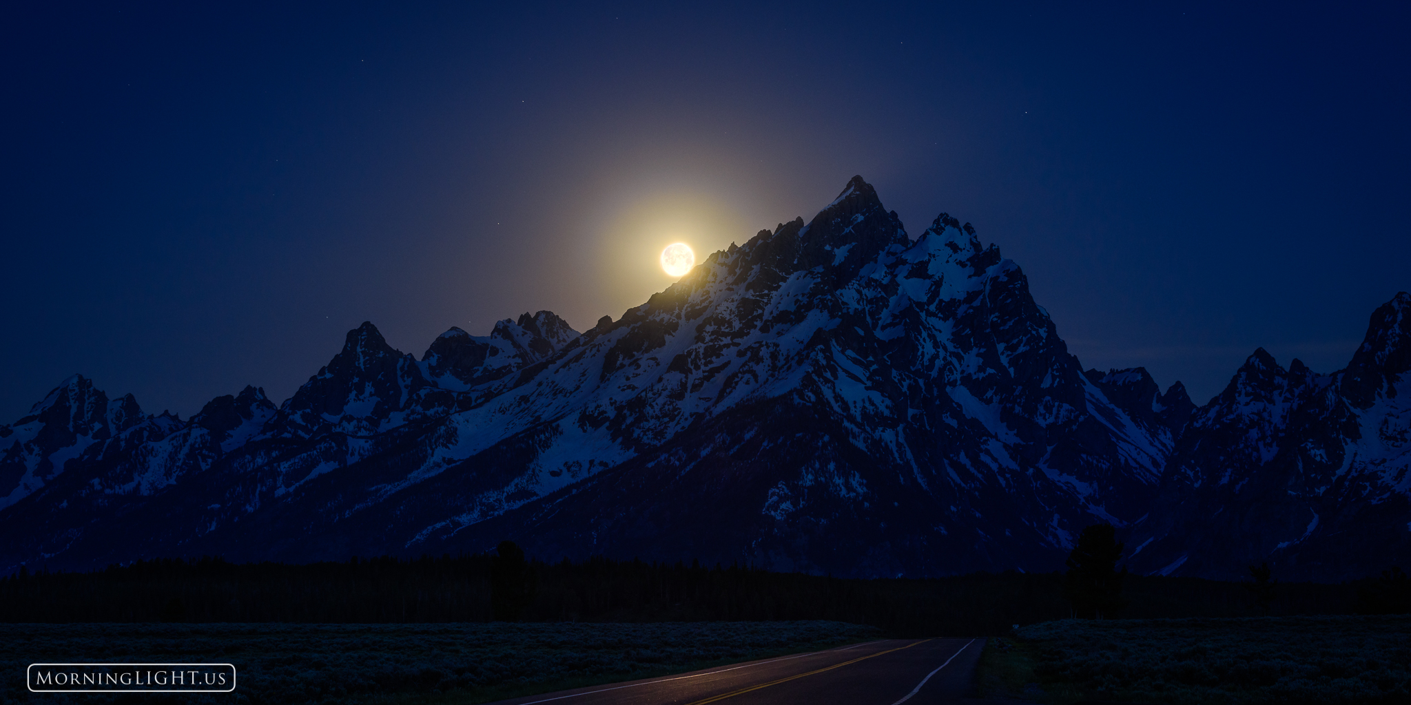 The national park highway heads right towards the dramatic Grand Teton in Grand Teton National Park, Wyoming as the moon sets...