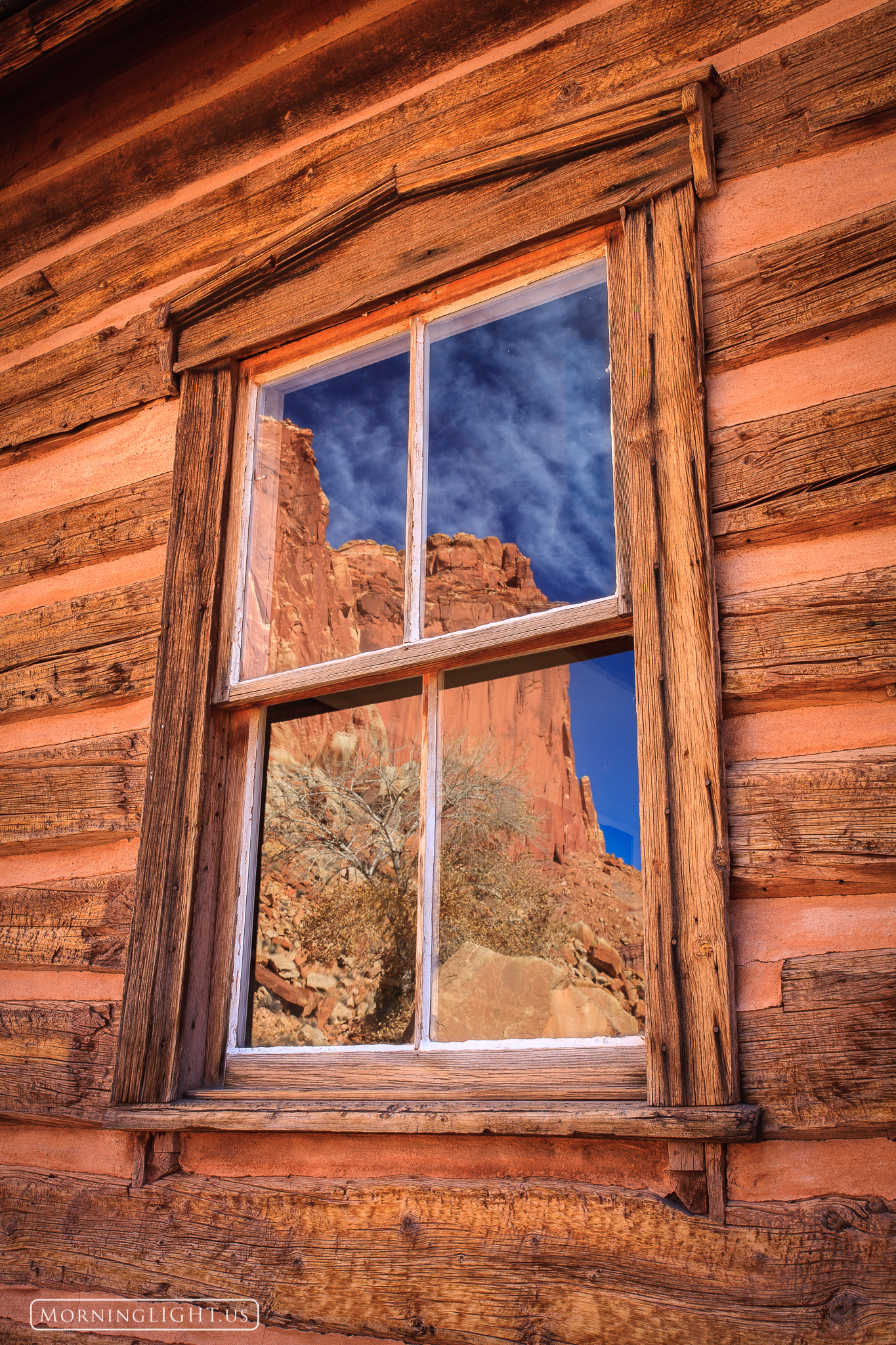 A large butte and clouds are reflected in the window of an old school along the road in Capitol Reef National Park in Utah.